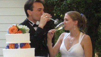A bride and groom drinking from a glass of wine.