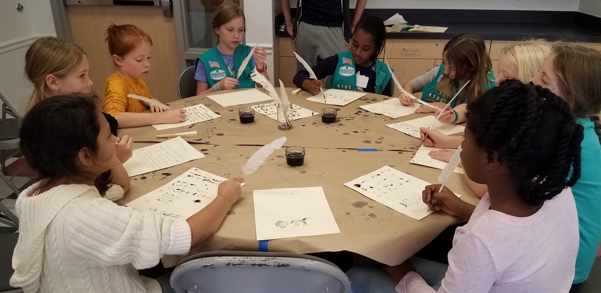 A group of girls sitting around a table and writing.