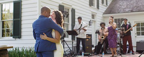 A bride and groom hugging in front of a white house.